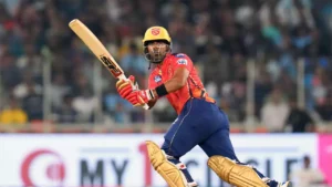 Shashank Singh in a red shirt and blue pants holding a bat